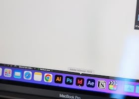 A detailed view of a MacBook Pro displaying Adobe InDesign and other design tools on screen.